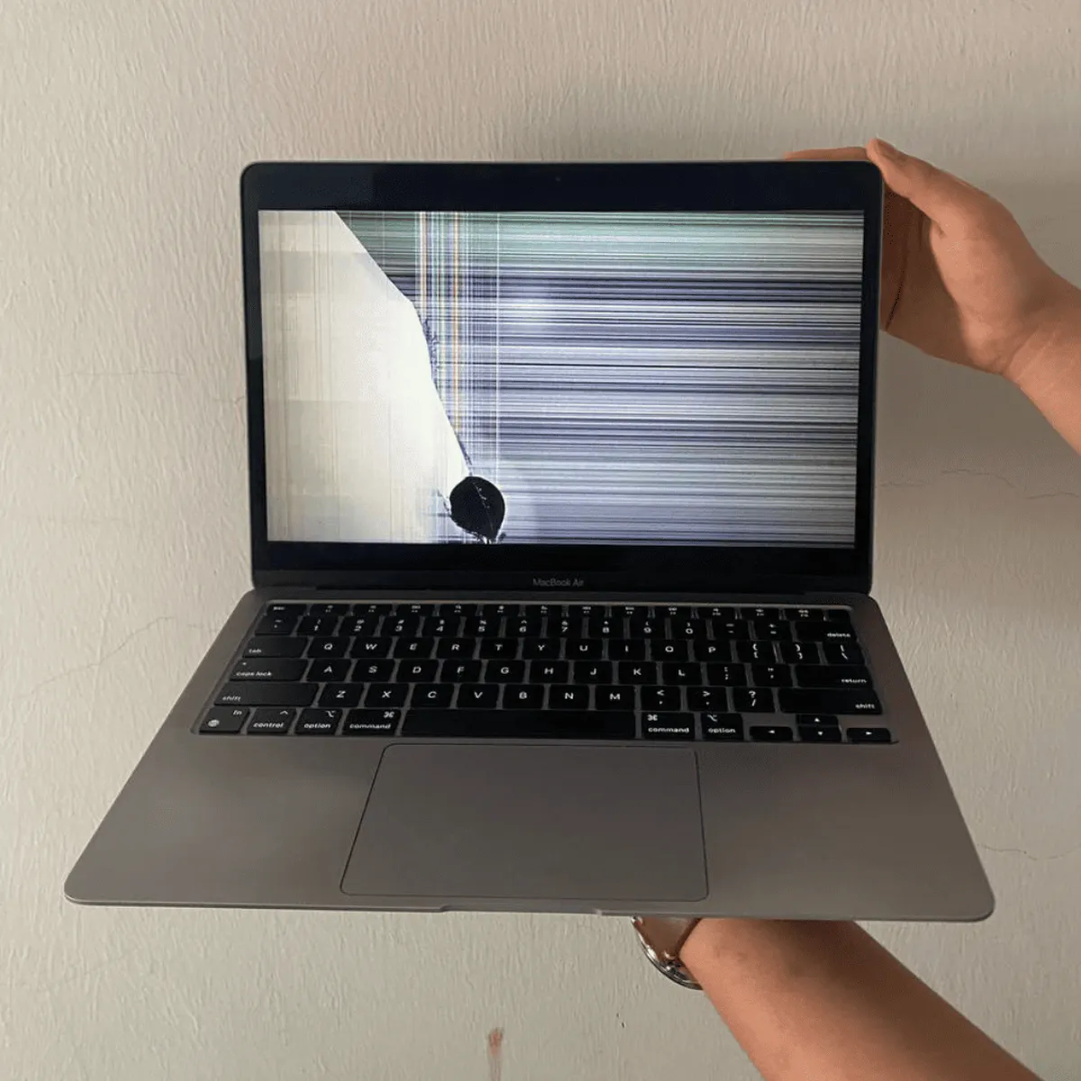 A MacBook Air powered on showing vertical lines and a cracked panel — a display assembly failure